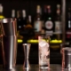 Does your business require a Liquor Licence and how do you apply for one? Picture of a bar with cocktail shakers and ornate glasses lined up in a row. Rows of alcoholic drink bottles lined up in the background.